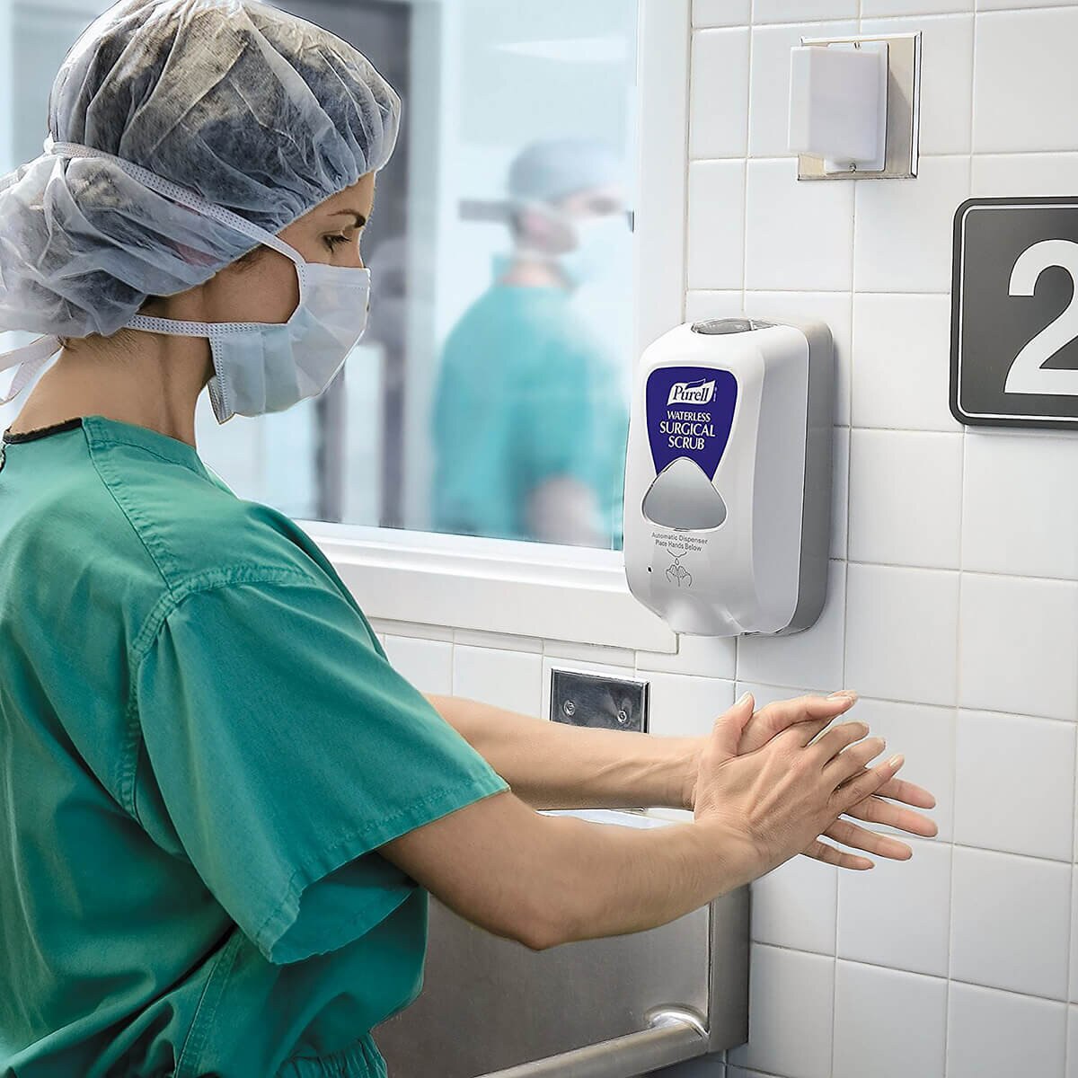 Healthcare professional using a wall-mounted Purell Waterless Surgical Scrub automatic dispenser in a clinical setting.